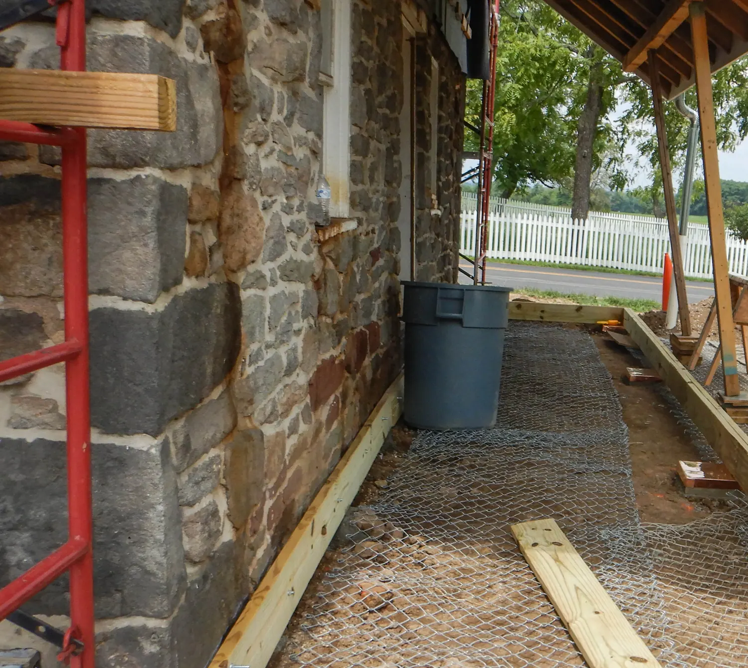 A new treated perimeter frame set out on the ground beside an old stone wall.