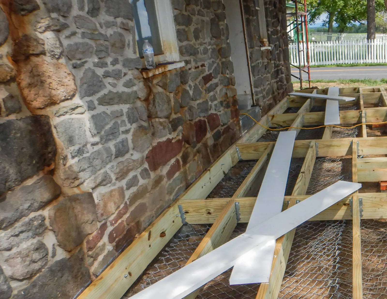 Pressure-treated joists hung off a ledger board fixed to a stone house wall.