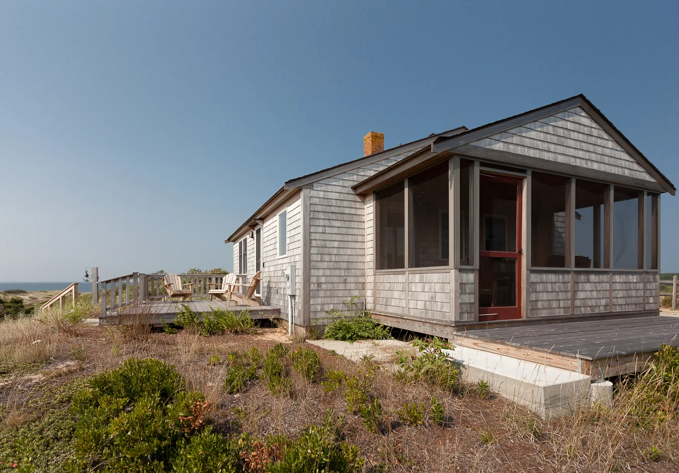 A shingled cottage with a screened porch at one end and an open deck beside it.